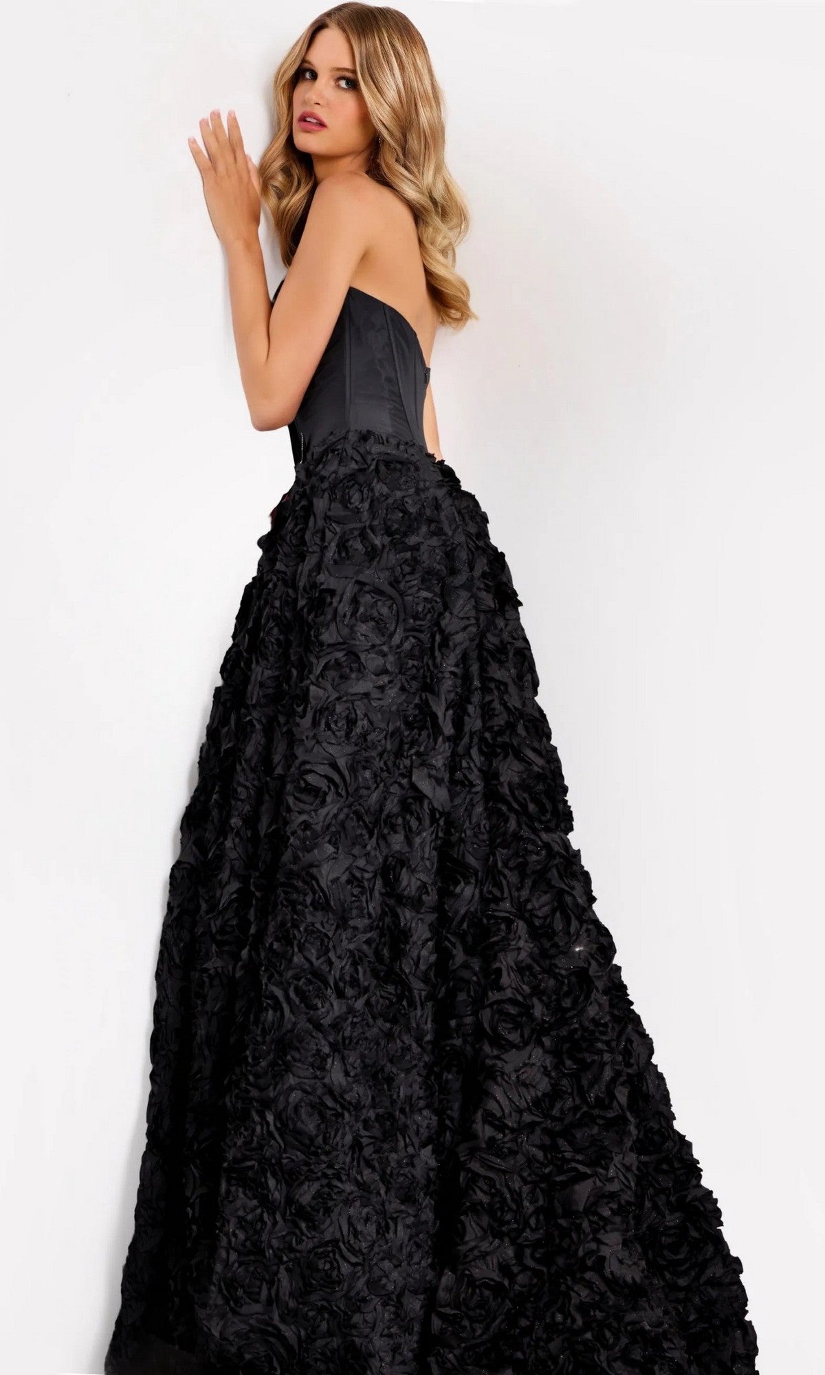 A woman stands against a plain white background wearing the Jovani 47695 long prom dress, which features a strapless corset bodice and a dramatic 3D rosette skirt.